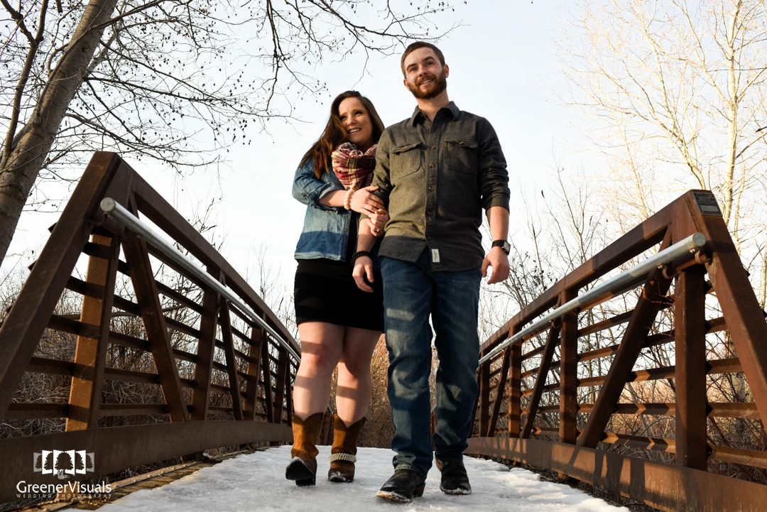 couple-walking-on-bridge-in-Bozeman-Story-Mill-Park-Winter-Engagement-Portrait