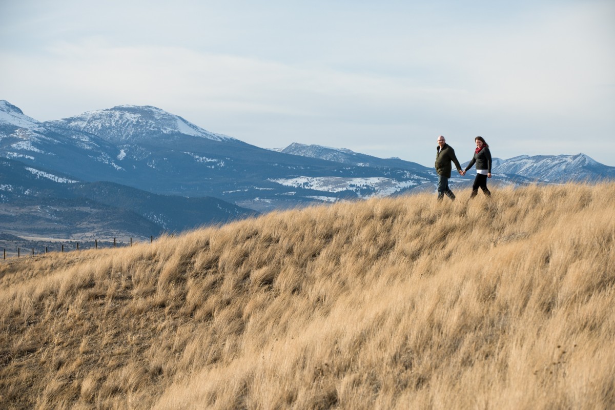 couple-walk-grassy-mountainside-during-Ennis-Montana-Engagement-Photos
