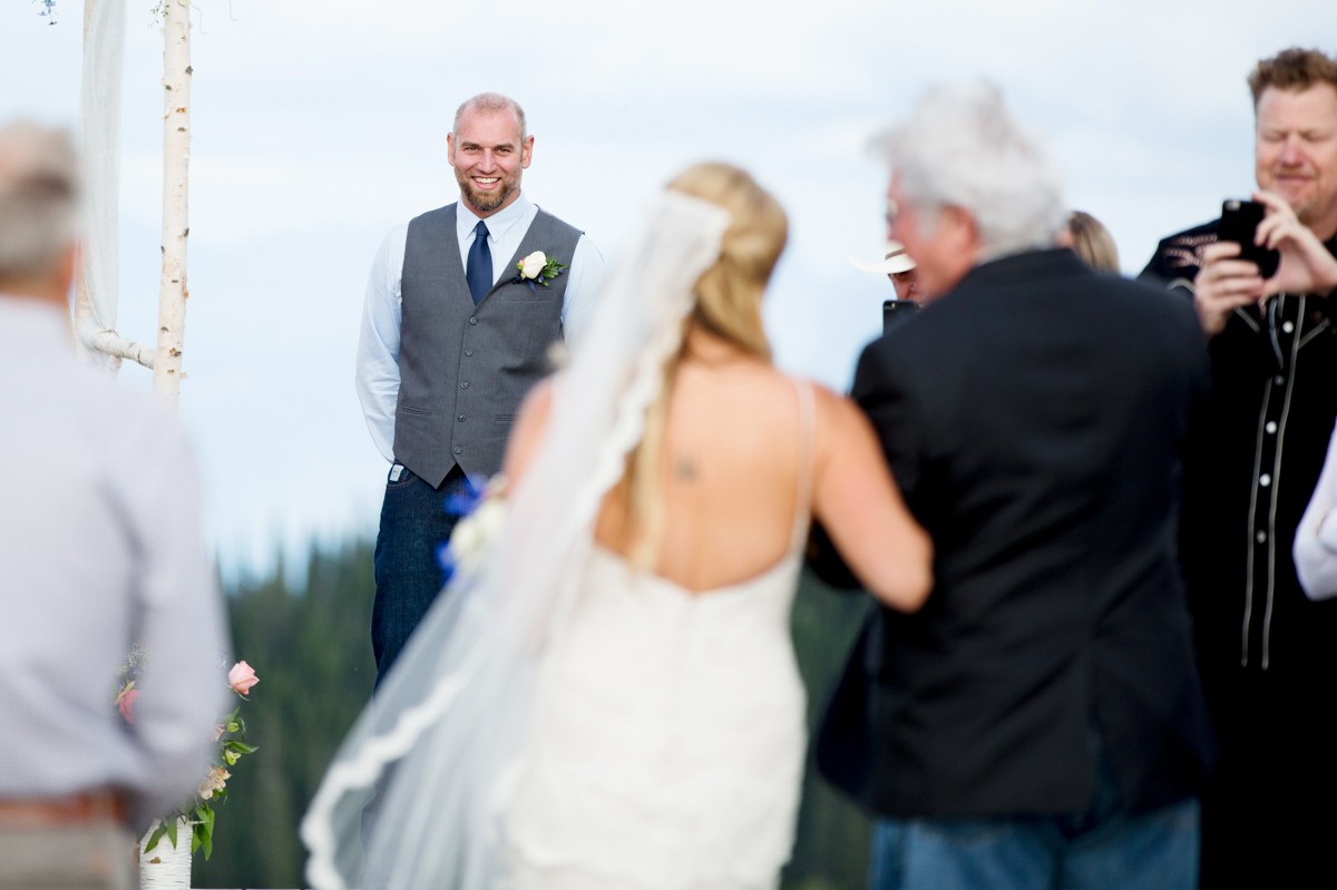 groom-smiles-watching-his-bride-walk-aisle-during-Whitefish-Mountain-Resort-Wedding