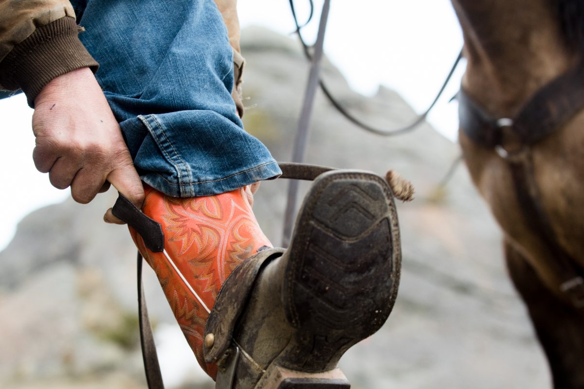 cowboy-puts-on-orange-boots-Horseback-Riding-Engagement-Portraits
