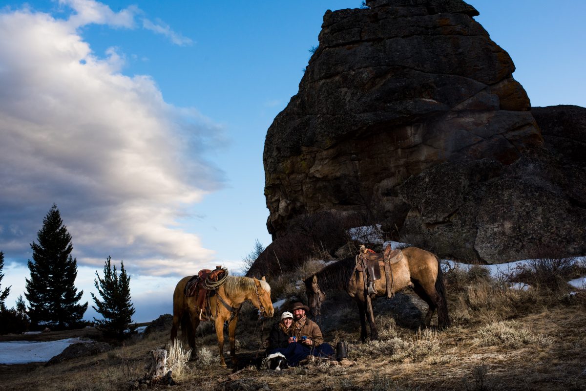 cowboy-couple-drink-coffee-by-fire-in-western-landscape-during-Horseback-Riding-Engagement-Portraits