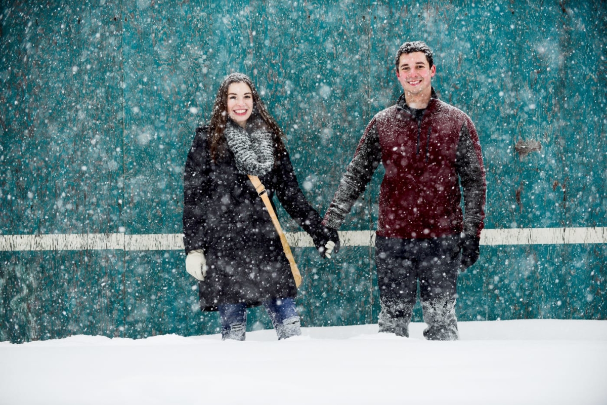 couple-holding-hands-against-teal-wall-during-snow-storm