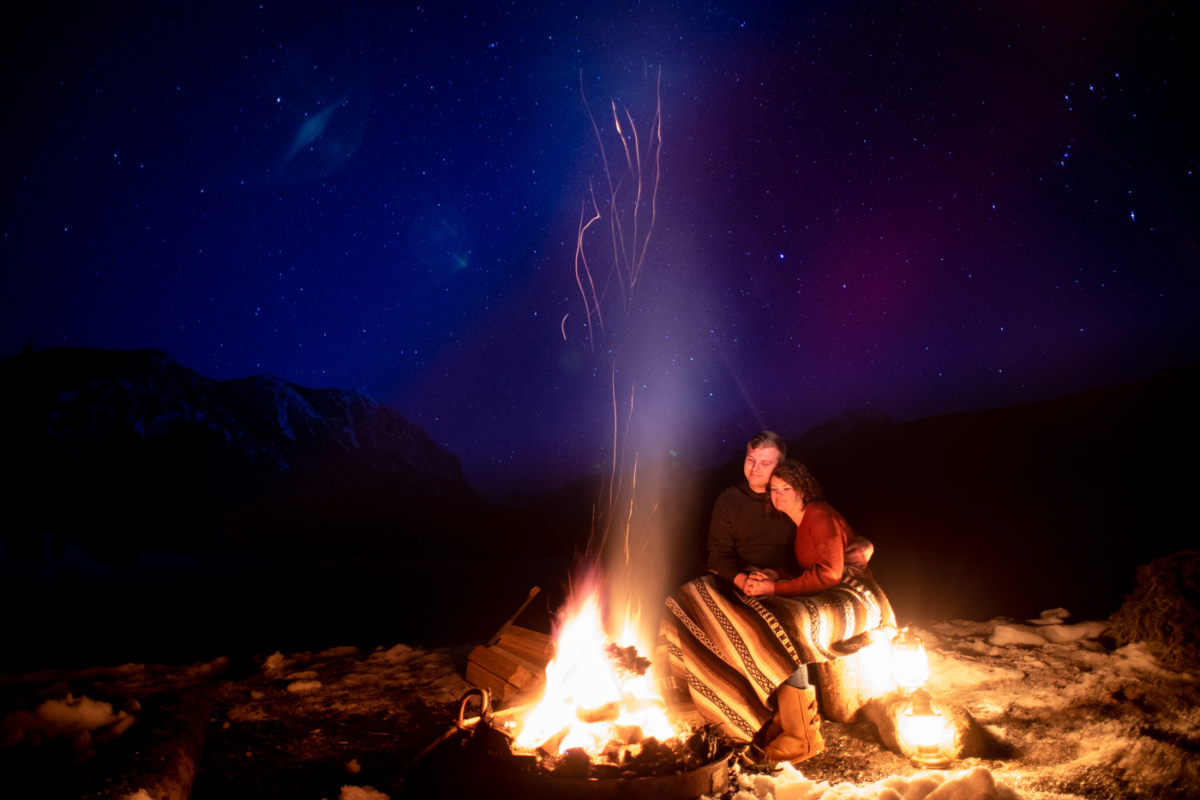 engaged-couple-embrace-around-campfire-during-Hyalite-stargazing-engagement-portraits