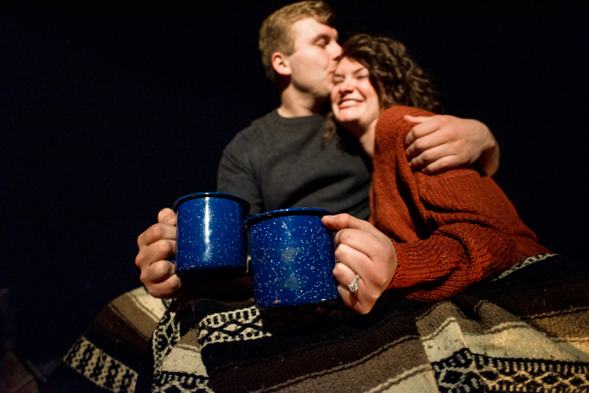 engaged-couple-drink-hot-chocolate-at-campfire-during-Hyalite-stargazing-engagement-portraits