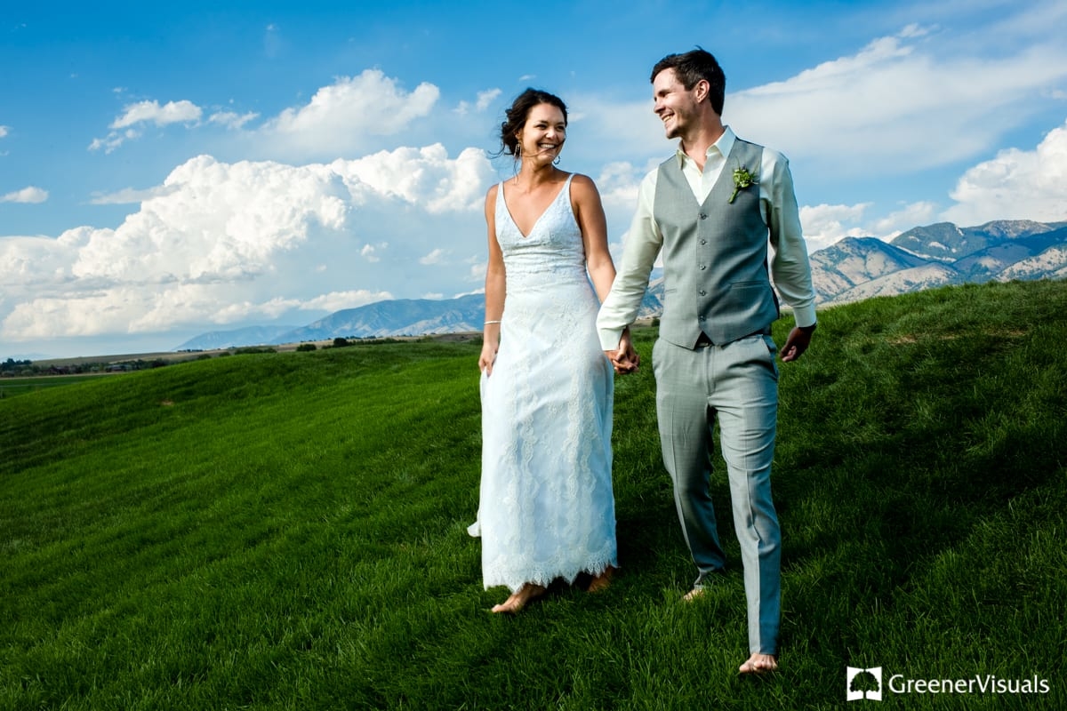 wedding-couple-walks-through-green-mountain-landscape-during-Countryside-Bozeman-Montana-Wedding