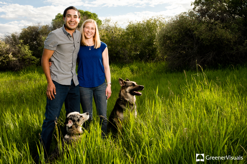 engaged-couple-with-dogs-stand-in-golden-hour-light-along-East-Gallatin-River