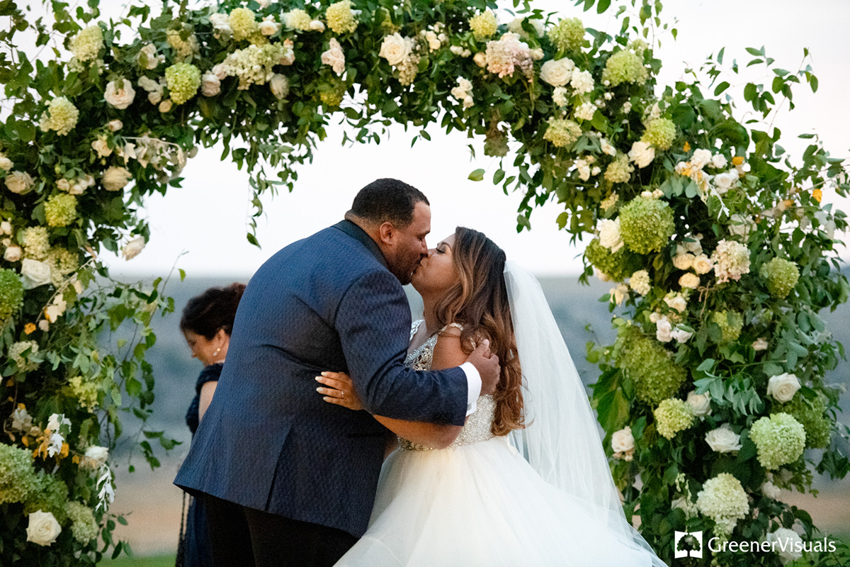 newlyweds-kissing-under-flower-archway