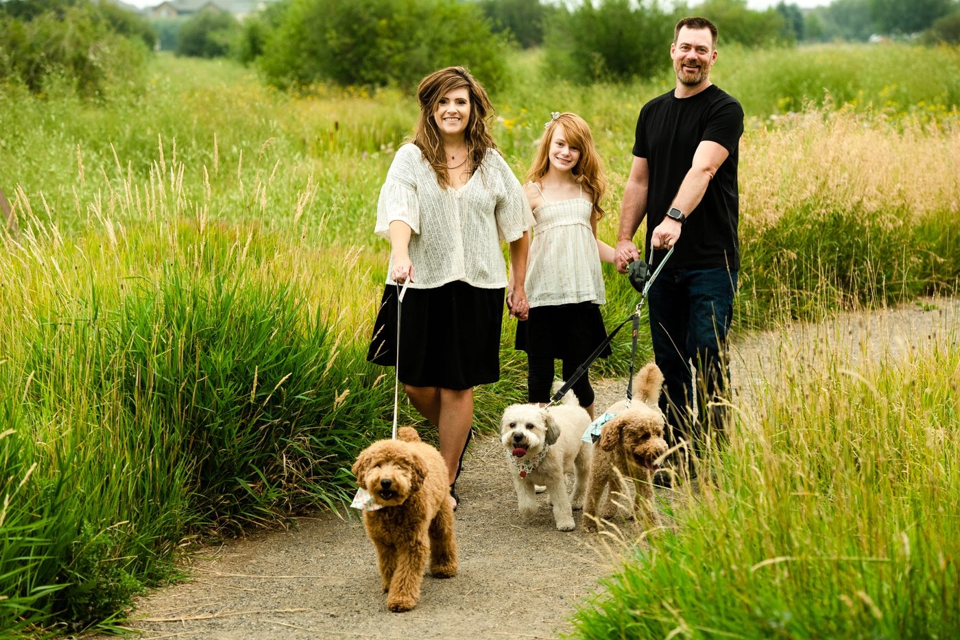 Parents-walk-with-daughter-and-dogs-in-green-grass-field