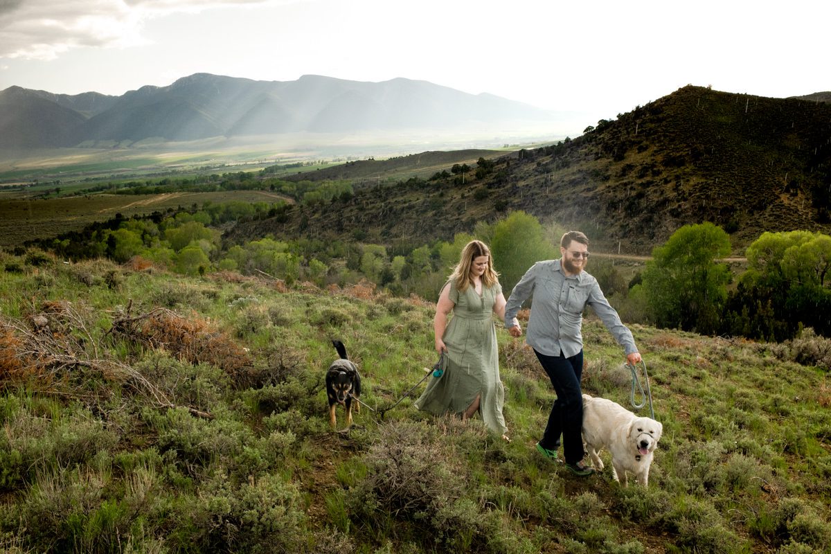 couple-walking-on-green-mountain-side-during-Montana-Ruby-Valley-Rainstorm-Engagement
