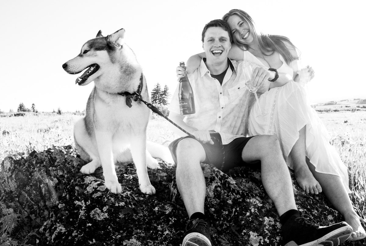 young-couple-with-dog-drinking-champagne-during-Mount-Ellis-Trailhead-engagement-portraits